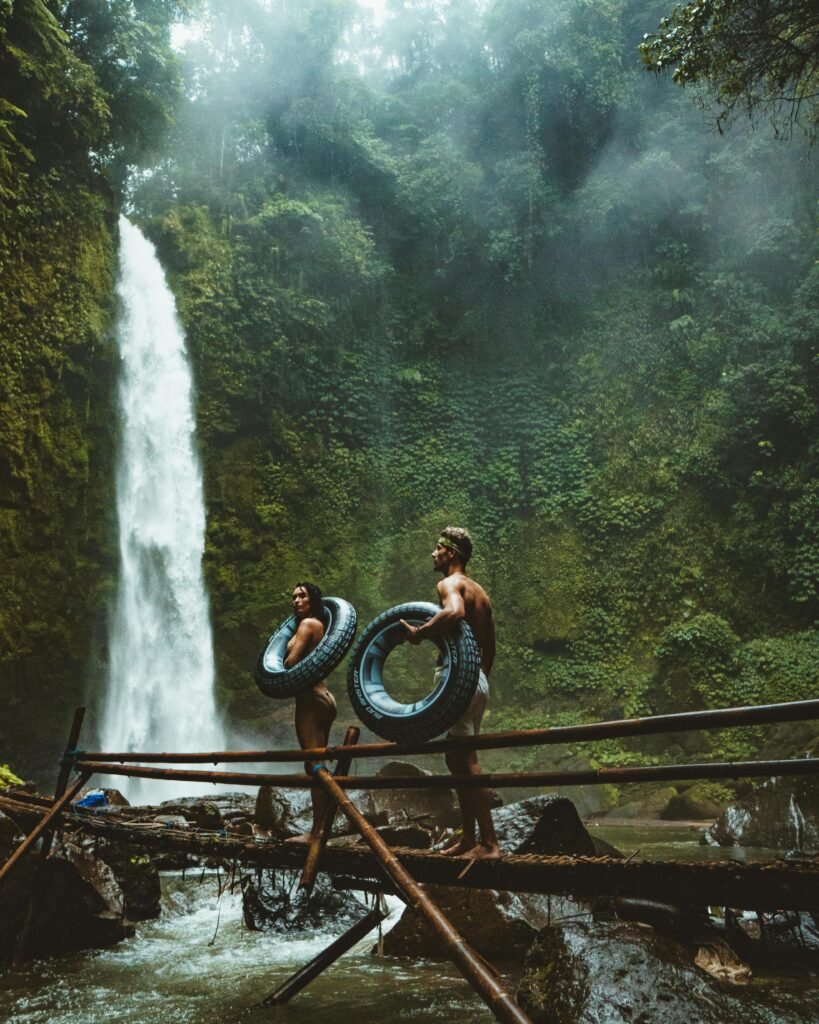 two-person-carrying-black-inflatable-pool-float-on-brown-wooden-bridge-near-waterfalls-